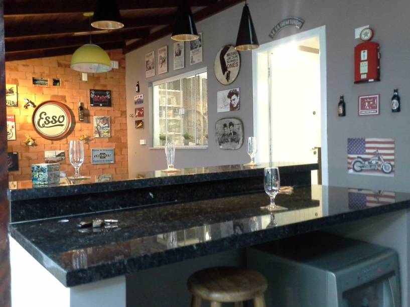 Os tijolos maciços foram colocados neste ambiente de 3,5 x 6,8 m para dar a sensação do morador estar em um pub. Eles também receberam acabamento de resina. Já as paredes foram pintadas em tons de cinza. O projeto é assinado pela arquiteta Cidia Nára Queluz Oriques para uma casa em Blumenau (SC).