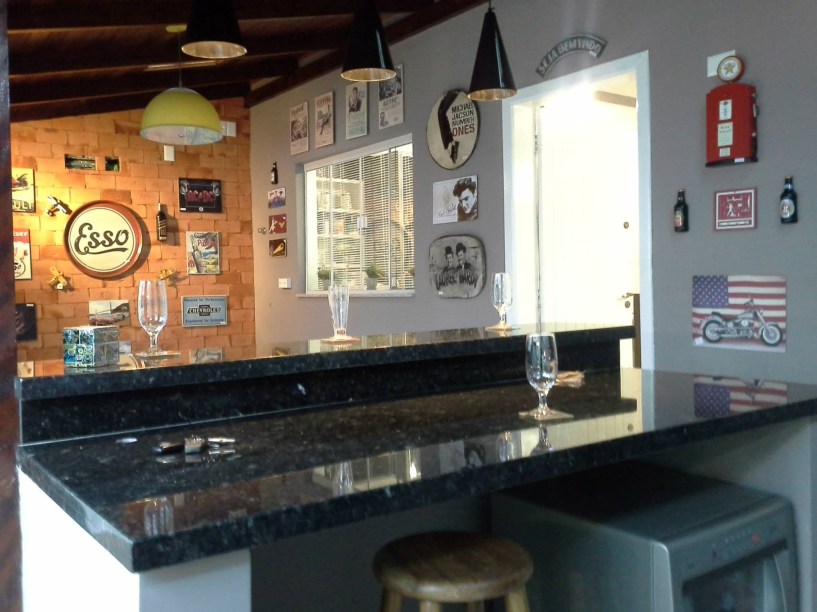 Os tijolos maciços foram colocados neste ambiente de 3,5 x 6,8 m para dar a sensação do morador estar em um pub. Eles também receberam acabamento de resina. Já as paredes foram pintadas em tons de cinza. O projeto é assinado pela arquiteta Cidia Nára Queluz Oriques para uma casa em Blumenau (SC).