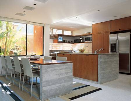 12 m&sup2;: O foco na praticidade fez os moradores rec&eacute;m-casados aproximarem a cozinha da sala de jantar. Eles curtem elaborar pratos juntos, diz o arquiteto Mario Gallo, de S&atilde;o Paulo. Apoio para o preparo, a bancada central tem tampo de aglomerado sint&eacute;tico e base de concreto tratado com resina. O mesmo material sustenta uma prancha de ip&ecirc; na mesa de refei&ccedil;&otilde;es. A mistura ponderada dos elementos de aspecto frio com a madeira clara resultou em um ambiente acolhedor e superatual, conclui Mario. Sobre o piso de granilite, o tapete de vinil e poli&eacute;ster tem um rasgo certeiro para encaixar o &uacute;nico p&eacute; da mesa.