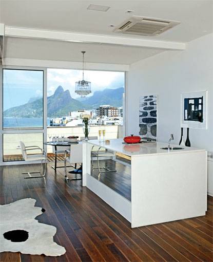 22 m&sup2;: A vista do mar e do morro Dois Irm&atilde;os determinou o projeto da arquiteta carioca Roberta Moura para esta cobertura: de olho na paisagem, ela cercou o espa&ccedil;o com pain&eacute;is de correr de vidro. E, ao criar um ambiente &uacute;nico de estar, destacou a cozinha gourmet  delimitada pela ilha de 2,30 x 1,10 m, revestida de m&aacute;rmore branco extra, que acomoda uma cuba de a&ccedil;o inox e um fog&atilde;o cooktop. O piso de t&aacute;buas de ip&ecirc; com 10 cm de largura foi aproveitado do deck que cobria o antigo terra&ccedil;o e intercalado com pequenas ripas de garapa. Ele resiste bem aos p&eacute;s molhados de quem sai da ducha existente na parte descoberta, garante Roberta.