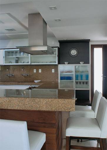 18 m&sup2;: Hobby do propriet&aacute;rio, a culin&aacute;ria ganhou espa&ccedil;o nobre neste projeto em que est&eacute;tica e funcionalidade convivem no mesmo plano. A integra&ccedil;&atilde;o com o living, absoluta, determinou o primor em cada detalhe, caso do raro granito am&ecirc;ndola dourado, que se estende pelas paredes e forma bancadas. No bloco maci&ccedil;o que embute o cooktop, a pedra conquista leveza com frisos em baixo-relevo. J&aacute; o limite entre as &aacute;reas &eacute; sutil: O p&eacute;-direito da cozinha mede 2,55 m, enquanto o restante do ambiente tem o gesso rebaixado em 20 cm, diz a arquiteta F&aacute;tima Basto, de Salvador. Pintada de berinjela, a parede do fundo tem nichos para armazenar vinhos.