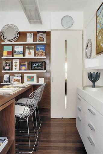 12 m&sup2;: Parece sala, mas &eacute; cozinha. Revestido de t&aacute;buas corridas de peroba-do-campo (com verniz fosco) e pintura branca nas paredes, mesmos acabamentos do restante do apartamento, o ambiente funciona como um prolongamento do living. Id&eacute;ia do arquiteto carioca Luiz Marinho, que desenhou inclusive os arm&aacute;rios, habitados por simp&aacute;ticos ping&uuml;ins, e a bancada de refei&ccedil;&otilde;es para duas pessoas. N&atilde;o queria nada padronizado, justifica. N&atilde;o por outra raz&atilde;o, ele tamb&eacute;m tra&ccedil;ou a estante onde ficam organizados os livros de culin&aacute;ria. A porta com detalhe vazado acrescenta gra&ccedil;a ao conjunto.