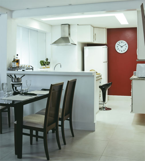 Na reforma deste apartamento, uma parede derrubada integrou a cozinha a sala. Ao lado da bancada de MDF, placas de porcelanato no piso integram os ambientes. A decoração clean é contrastada pelo vermelho da parede.