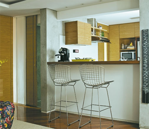 Neste apartamento de 80 m², a madeira prevalece em todos ambientes, unificando-os. A integração da cozinha com a sala fica por conta da bancada de ipê, que disponibiliza ainda dois lugares para refeições. As arquitetas Adriana Cocchiarali e Isabela Jock Piva assinam esta reforma.