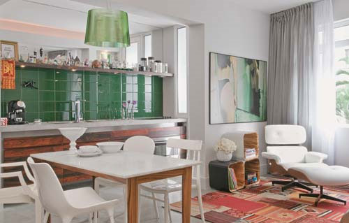 Neste apartamento de 57 m², cozinha e sala é uma coisa só. As áreas são diferenciadas pelas cores marcantes, como o verde escuro do azulejo da cozinha. O contraste fica por conta do tapete da sala, em tons quentes.
