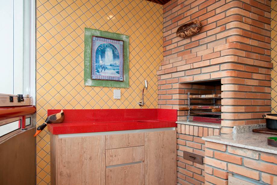 Na área de churrasqueira de 6,7 m², os tijolos aparentes foram colocados na obra pela própria construtora. O trabalho da arquiteta e designer de interiores Helen Granzote foi tornar o ambiente mais colorido. Para isso, ela optou pela pedra quartzo vermelho Stellar para a pia e a substituição do piso convencional por um mosaico de cerâmica ecológica da marca Lepri. O projeto é para uma residência em Santo André (SP).