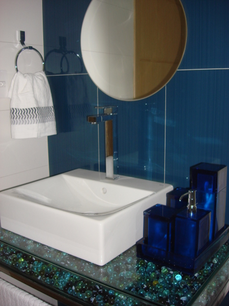 A bancada em vidro tipo caixa, cheia de bolinhas de gude, é o destaque deste banheiro, projetado pela arquiteta Janete Barros para um menino de nove anos de idade. As cores em degradê das bolinhas combinam com o tom azul, escolhido para o revestimento da parede. O espaço é de 4,5 m² é de uma residência em Arapiraca (AL).