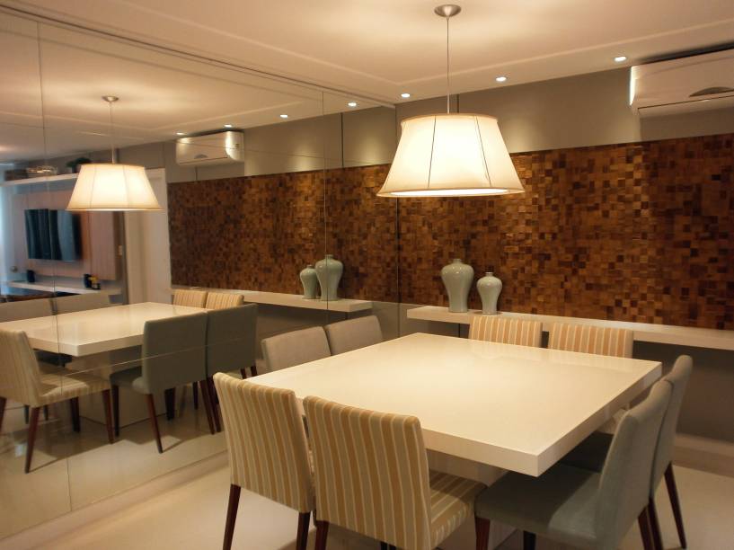 Painéis de espelho revestem as paredes, tornando a sala de jantar deste apartamento em São José (SC) mais ampla visualmente. “O brilho a e luz do acabamento em laca e vidro branco na mesa reforçam o conceito contemporâneo, enquanto os tecidos lisos e listrado nas cadeiras trazem movimento”, explica a designer de interiores Marina Sá.