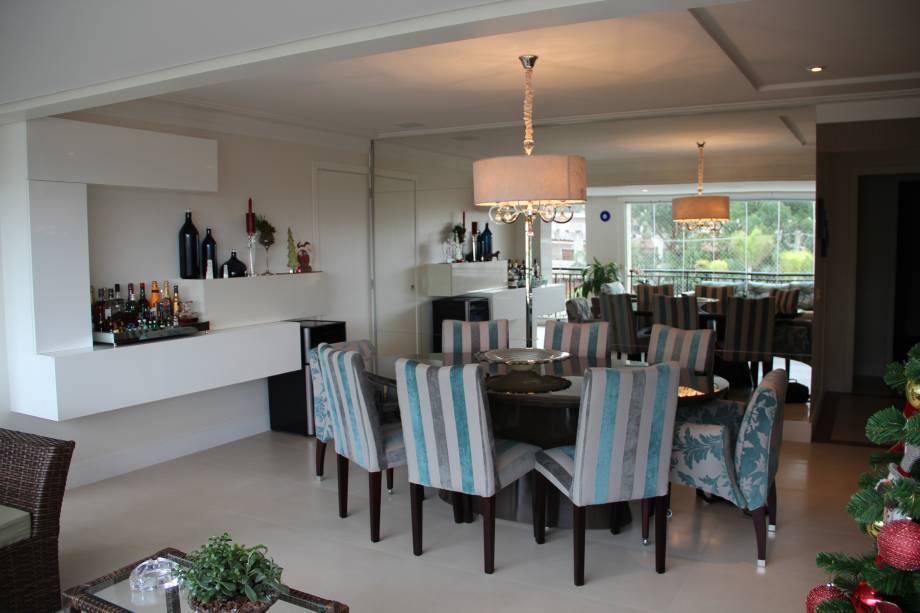 Piso em porcelanato padrão mármore Crema Marfil, paredes e bar em laca off-white, mesa de jantar em laca marrom e estofados em cinza e azul turquesa formam a sala de jantar de 17 m² deste apartamento em São Paulo (SP). “As portas de vidro da varanda foram retiradas, integrando a sala de jantar com o living, varanda e espaço gourmet”, explica a arquiteta Paula Nicolini, que assina o projeto.