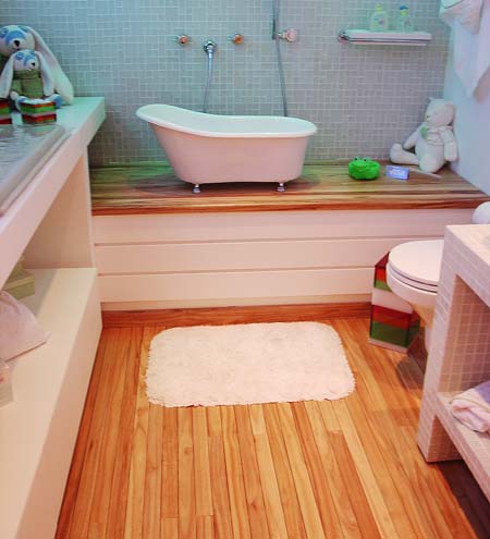Todo o chão do banheiro do bebê é revestido com um deck de madeira envernizado para poder entrar em contato com a umidade. O deck é espaçado e possui ralos na parte de baixo. Assim, depois que o bebê tomar banho, dá para jogar a água direto no chão.