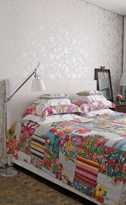O fundo branco da cabeceira e do papel de parede, combinados aos m&oacute;veis de madeira, permitem ousar nas estampas. A do papel (Miranda Green) combina com o floral da roupa de cama (Villa Nova). O quarto foi decorado pela designer de joias Brenda Vidal.