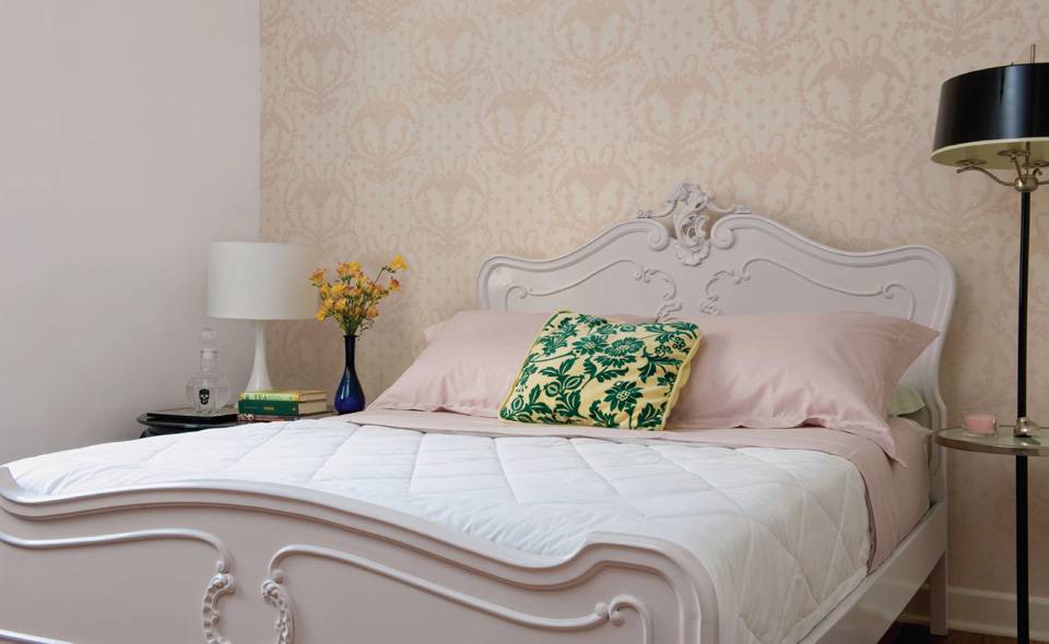 Para aproveitar a cama antiga comprada numa loja de usados, a pintura original (verde-claro com frisos dourados) foi trocada pelo off-white. Assim, o m&oacute;vel se encaixou bem na decora&ccedil;&atilde;o neutra do quarto, que permitiu uma lumin&aacute;ria de p&eacute; com c&uacute;pula preta, original dos anos 1950 (Heran&ccedil;a Cultural), e a almofada verde e amarela. Roupa de cama da Trousseau. O projeto &eacute; assinado pelo designer de interiores Omar Assais.