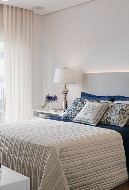 Revestimentos claros ajudaram a fazer o quarto decorado pelas arquitetas Fernanda Morato e Marcia Monteiro parecer ter mais do que seus 14 m2. Para n&atilde;o perder aconchego, um papel de parede com textura de tecido vestiu as paredes. O revestimento, da Wallpaper, combina com a cabeceira de camur&ccedil;a sint&eacute;tica da Regatta (execu&ccedil;&atilde;o da tape&ccedil;aria Moreno M&oacute;veis). Enxoval da Trousseau e almofadas da Ana Luiza Wawelberg.