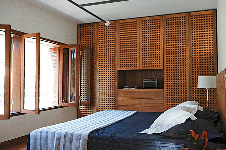 A combina&ccedil;&atilde;o de paredes claras e m&oacute;veis no tom de madeira natural cria uma combina&ccedil;&atilde;o neutra que se d&aacute; bem com detalhes de qualquer cor. Neste quarto, assinado pelo arquiteto Renato Marques com o s&oacute;cio Daniel Fromer, os arm&aacute;rios s&atilde;o o foco principal. Projetados pela designer Claudia Moreira Salles, eles ganharam portas treli&ccedil;adas feitas de freij&oacute;.