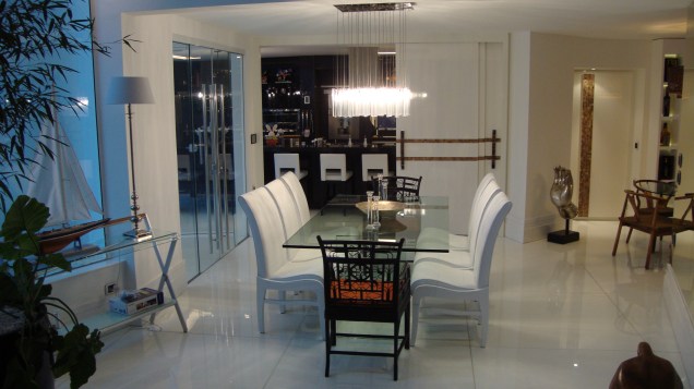 Nesta sala de jantar, piso em marmoglass, cadeiras em laca branca com estofado em couro branco e mesa de vidro compõem o espaço. O projeto é da arquiteta Rosane Aguiar.