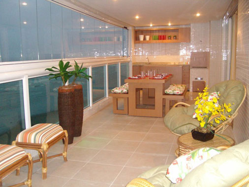 A varanda deste apartamento na praia é grande: ela mede 15 x 2,70 m. Com esta metragem, foi possível incluir uma churrasqueira. Deck, mesa, bancos, console e armários foram executados pela Marcenaria Nique (SP). Os móveis de rattan e os vasos de cerâmica, importados da Indonésia, foram fornecidos pela Uemura Flores e Plantas. Como o apartamento de veraneio não é visitado frequentemente, a designer de interiores Cristina Mussi escolheu plantas artificiais para a varanda uma vez que as naturais não receberiam os cuidados necessários.