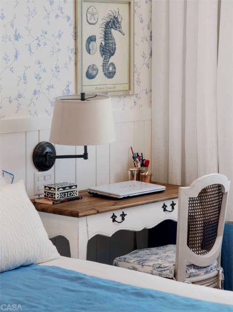 A lateral da cama acomodou, em vez do criado-mudo, um apoio para o notebook que segue o estilo do quarto, composto de mesa de madeira (Rug Hold) e cadeira com encosto de palhinha e almofada no assento (Elle et Lui Maison). Dessa mesma loja vem o quadro de cavalo-marinho.
