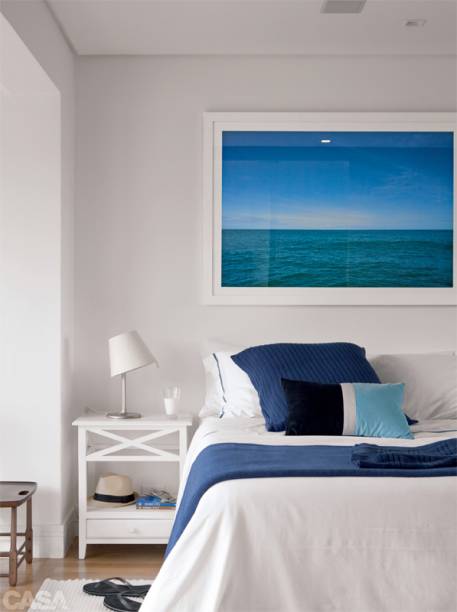 No quarto, roupa de cama e almofadão da Trousseau, almofada azul e preta de Ari Beraldin, luminária da La Lampe e tapete da Casa Fortaleza. Na parede, fotografia de Fran Parente. Ideia simples e funcional para quem não tem muito espaço ao lado da cama: um criado-mudo estreito. Com dois andares e uma gaveta, ele oferece área suficiente de apoio para os pertences do dia a dia. Projeto de Alessandro Bento.