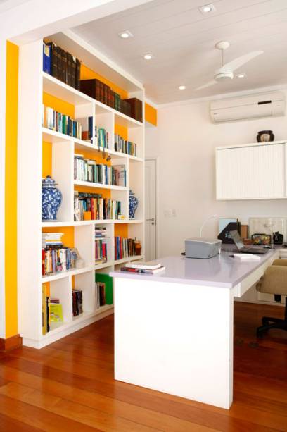 O home office projetado pela designer de interiores Simone Collet divide o espaço com a sala de estar, totalizando 12 m². Para um casal que ocasionalmente trabalha em casa, uma das preocupações da profissional foi colocar uma mesa para apoiar os notebooks. “Projetei uma canaleta para esconder a fiação da impressora e dos notebooks, assim não ficam fios pendurados”, conta.