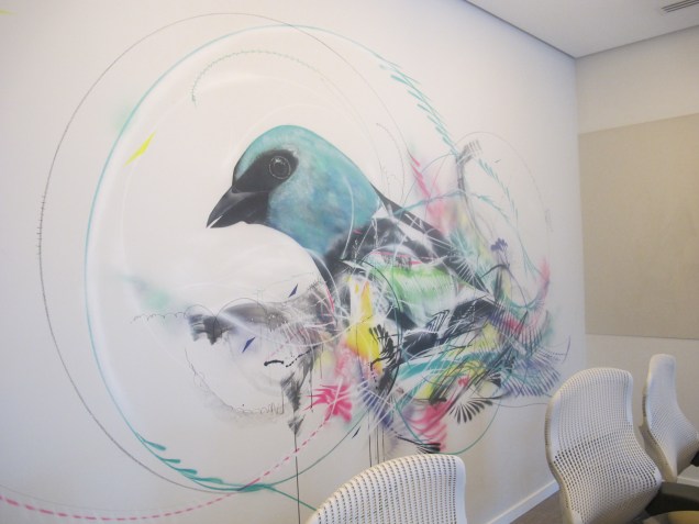 Pintura de um pássaro, símbolo da empresa, em uma das salas de reunião. A obra lembra os grafites espalhados pelas ruas de São Paulo.