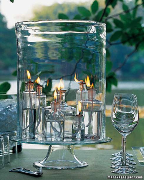 <span style="font-weight:400;">Para fazer suas próprias velas, junte algumas garrafas claras e preencha-as com óleo e pavios. Organize as garrafas dentro de um grande recipiente de vidro para proteger as chamas do vento.</span>