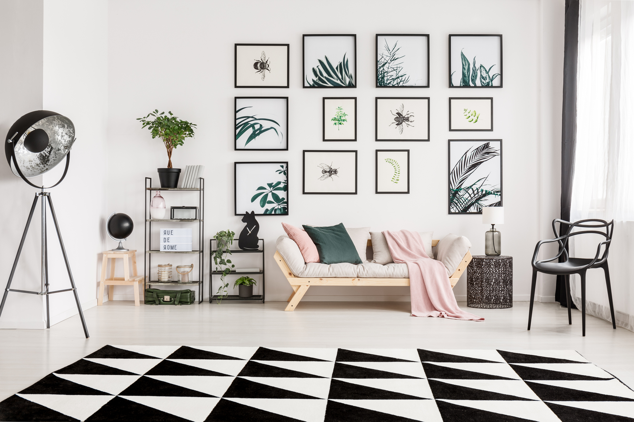 sala de paredes brancas com diversos quadros pendurados, tapete preto e branco e acessórios em cores claras