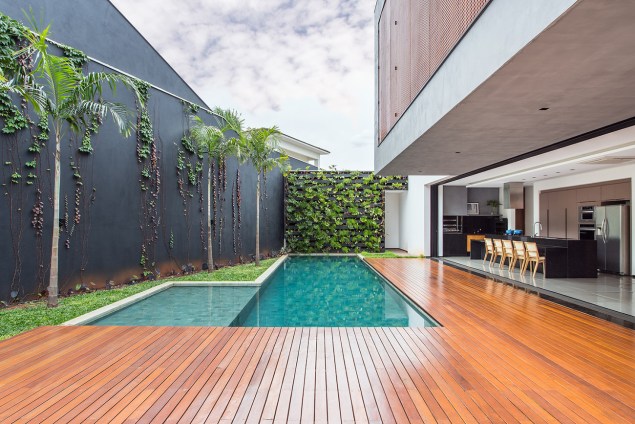 O projeto do escritório CF Arquitetura prioriza a integração entre os ambientes. Com portas de correr que ficam embutidas nas paredes, o living se abre para o deque da piscina, que conta com um grande jardim vertical.