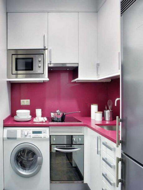 Nesta minicozinha, há espaço não só para os eletrodomésticos do ambiente como também para uma máquina de lavar roupas. A bancada e a rodabanca revestidas em um rosa vibrante trazem cor e personalidade para o espaço.