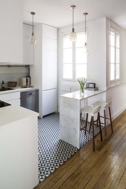 Como o apartamento parisiense, renovado por Anna Piwonska, tem pé direito alto, a cozinha sofisticada possui armários que vão até o teto. O piso limita visualmente o espaço, que conta com uma bancada para refeições.