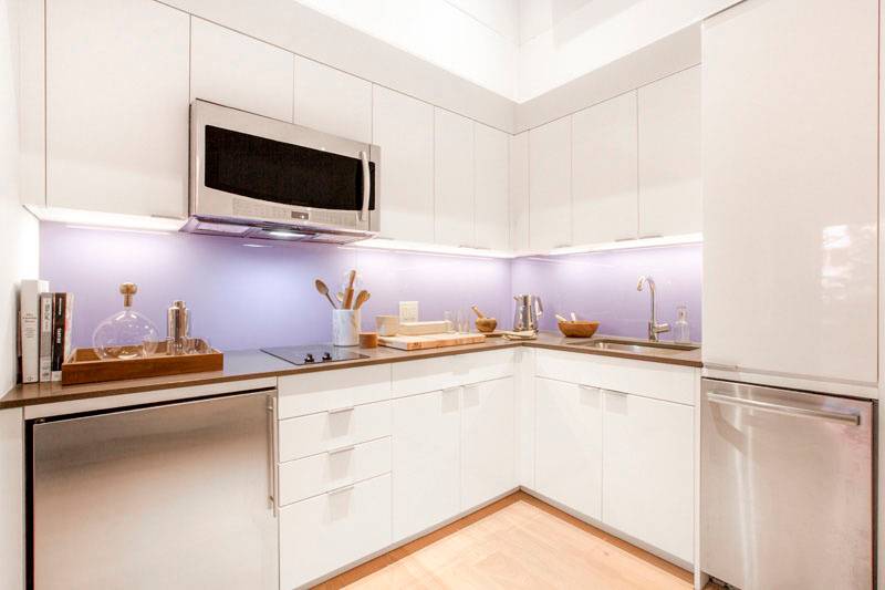 O segredo est&aacute; na ilumina&ccedil;&atilde;o: al&eacute;m das lumin&aacute;rias no teto, existem faixas de luz por baixo dos gabinetes que abrilhantam esta cozinha. Para trazer um toque de cor, o nicho entre arm&aacute;rio e bancada foi pintado de lavanda.