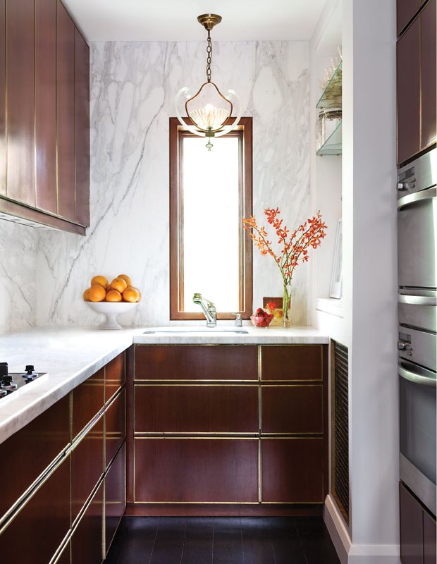 Esta cozinha em corredor possui uma bancada de mármore branco em formato de "L". Os contornos de bronze nas gavetas dos gabinetes também servem como puxadores.