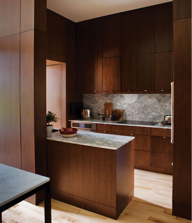 Revestida de madeira, esta cozinha apresenta contraste no balcão e no backsplash de mármore. Os materiais naturais aquecem o espaço e os armários, até o teto, alongam o pé direito.