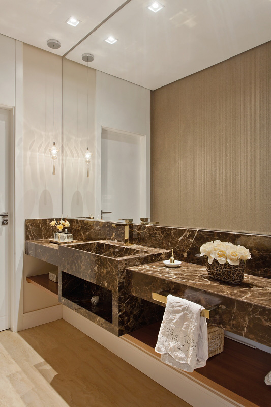 No lavabo, o espelho acompanha toda a extensão da bancada em mármore marrom imperador e duplica a delicadeza do papel de parede.
