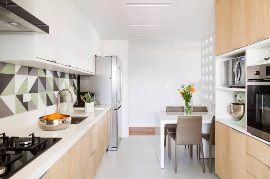 Na cozinha, armários brancos e de madeira se misturam compondo um décor leve e aconchegante. O backsplash com tons de cinza e verde e formas geométricas dão um tom moderninho ao espaço. Projeto da arquiteta Barbara Dundes