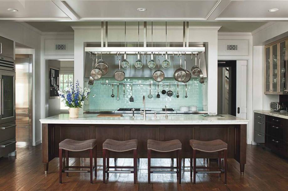 Esta casa de estilo neocolonial foi decorada pela designer Mariette Himes Gomez. A cozinha tem como destaque o backsplash azul turquesa, o único item colorido da decoração. A ilha de mármore traz detalhes do estilo clássico na parte de madeira e combina com os bancos do mesmo material e estofados de veludo