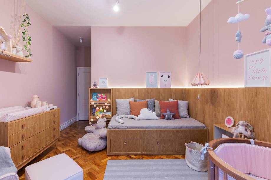 Também do escritório AS Design Arquitetura, este quarto de bebê foi totalmente reformado para receber a princesa da família. As profissionais fizeram um painel em madeira freijó que acompanha a parede da cama até a porta, com destaque para a fita de LED, que deixa o ambiente mais charmoso. O projeto de 14 m² foi criado pensando no uso futuro, com possibilidades de boas adaptações, como a saída do berço e cama da babá para a entrada de nova cama da criança, com escrivaninha.