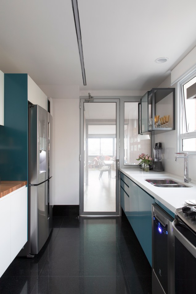 Comprida, a cozinha ganhou armários azuis e brancos, a fim de equilibrar o piso escuro também mantido na reforma.