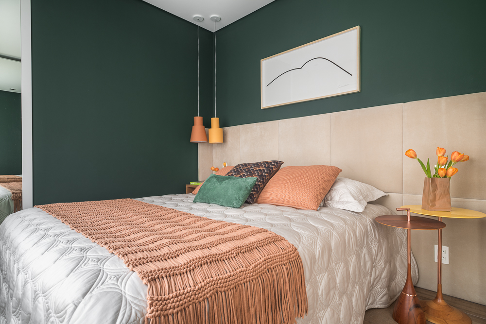 Quarto com parede verde; cama; cabeceira acolchoada; roupa de cama; duvet; almofadas coloridas; luminárias