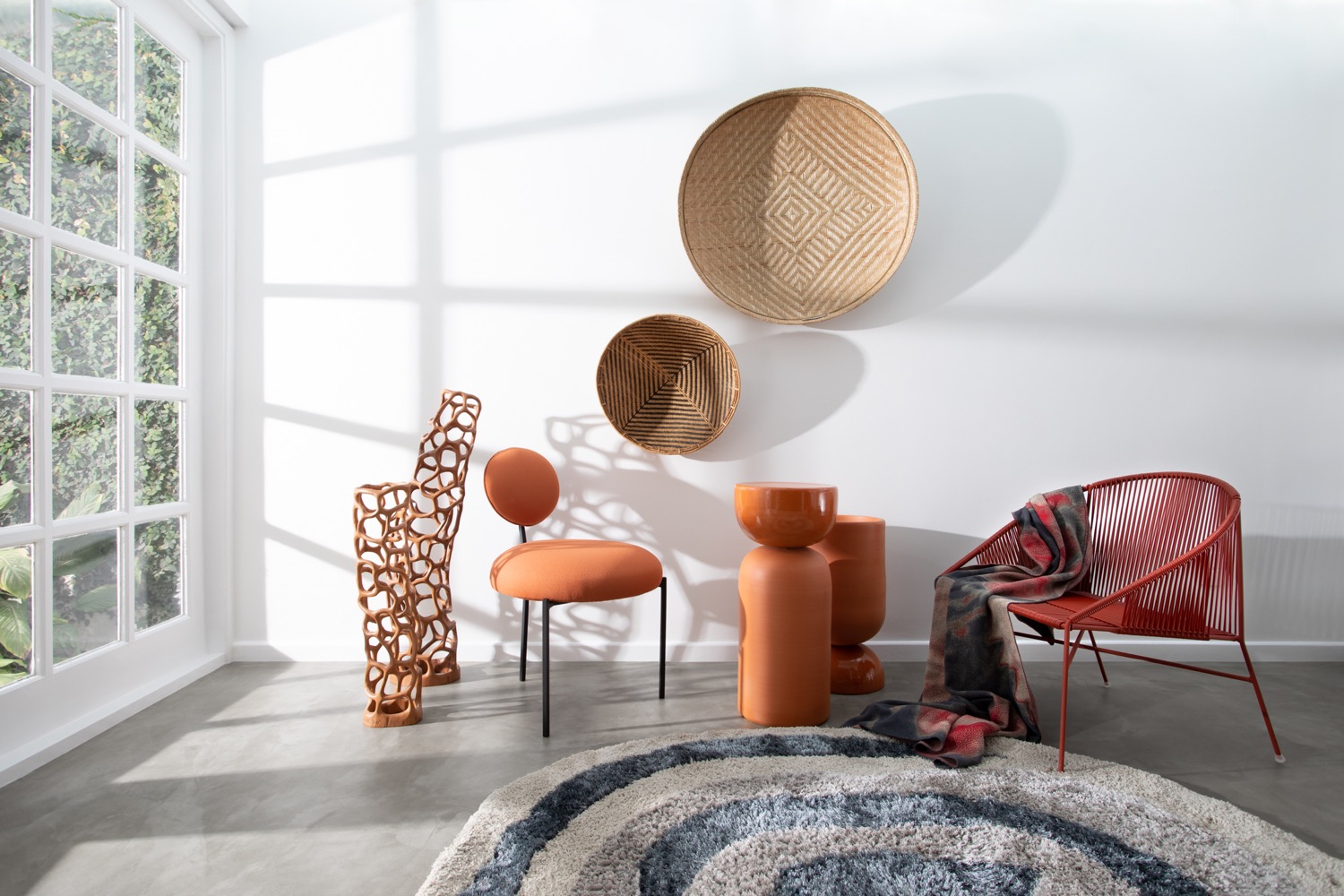 Sala com tapete circular, duas cadeiras arredondadas e cestas penduradas nas paredes