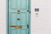 Fachada de uma casa com porta verde-água, parede de tijolinhos brancos e número 24
