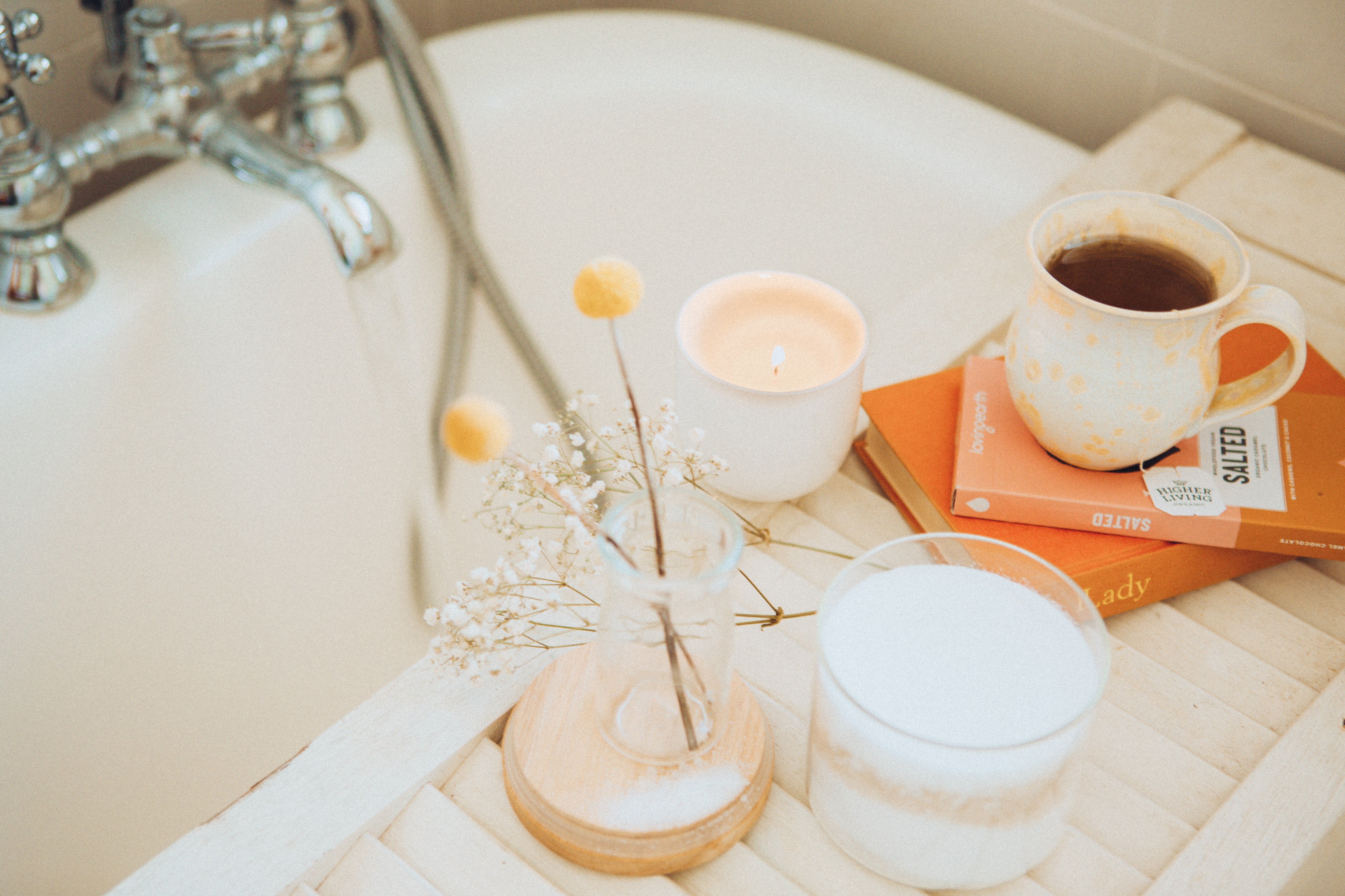 Velas, flores, livros e uma caneca de chá sobre um apoio de madeira em uma banheira de banho