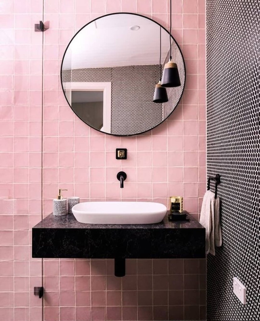 Banheiro com azulejos rosa; espelho redondo