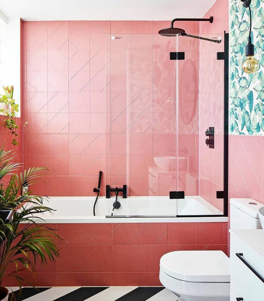 banheiro com revestimento rosa, box em vidro com detalhes pretos. 