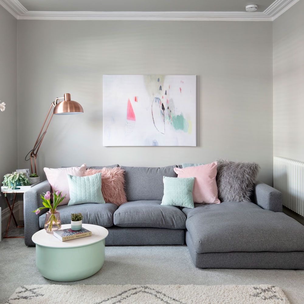 Sofá cinza com almofadas verdes e rosa; luminária de piso; quadro na parede
