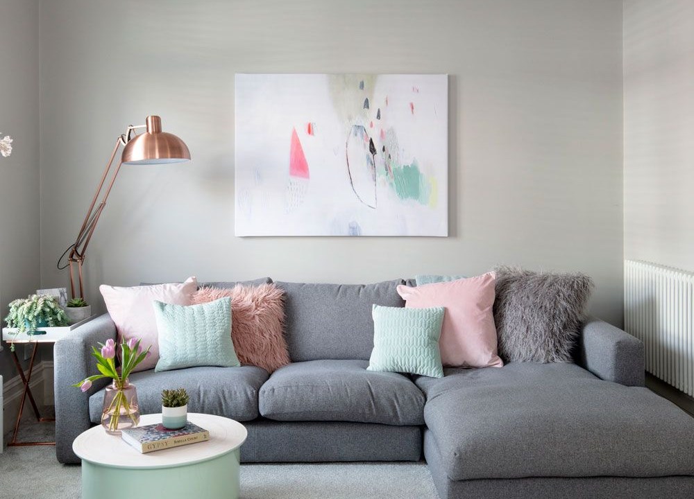 Sofá em L cinza; almofadas rosas e verdes; luminária de piso; quadro na parede