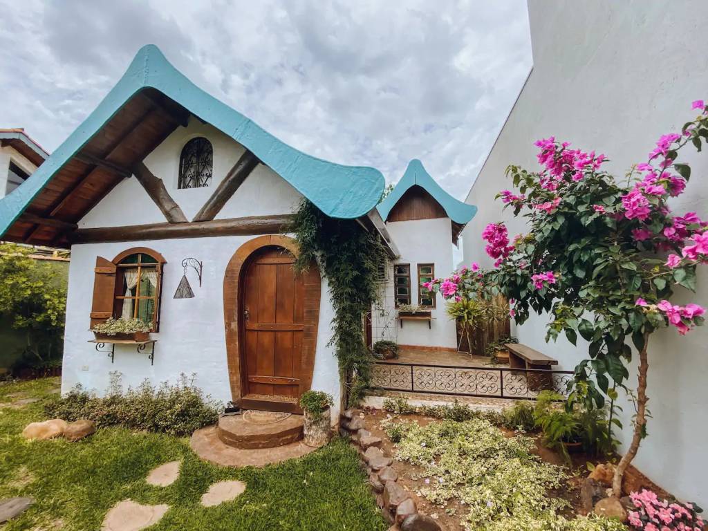 Casa de conto de fadas com parede branco, teto triangular de madeira, porta e janela com batente arredondado