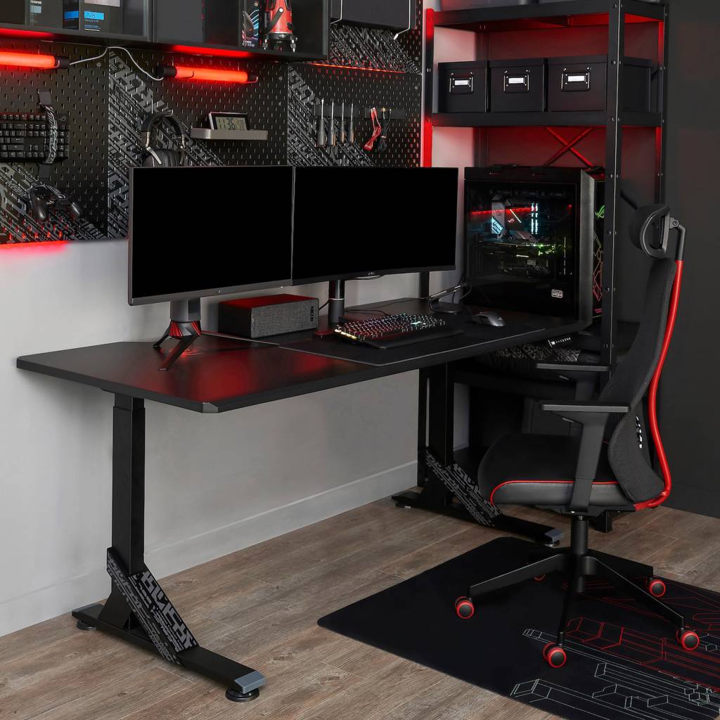 Mesa preta com dois monitores de computadors. Na parede, um mural com acessórios, como fone, teclado e ferramenta. Na lateral, uma estante com a CPU. E uma cadeira gamer com detalhes vermelho.