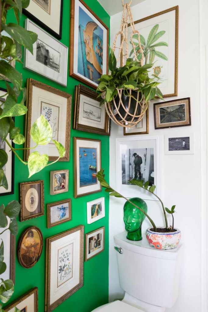 13-dicas-para-decorar-banheiros-pequenos-casa.com-10 Banheiro com uma parede verde vibrante cheia de quadros, com fotos e pinturas em molduras de madeira de diversos tamanhos