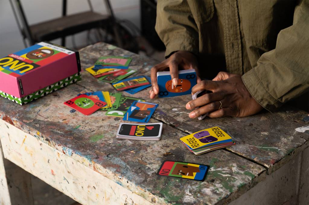 Cartas de UNO espalhadas em uma mesa de cimento queimado, com um par de mãos mexendo nelas