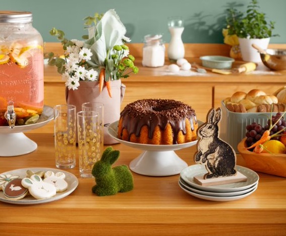 Mesa de páscoa em madeira com coelhinhos de enfeite, vaso com flores e bolo de cenoura